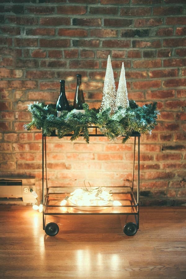 A garland sits on the top of the cart and the lights sit on the bottom, set against a brick wall
