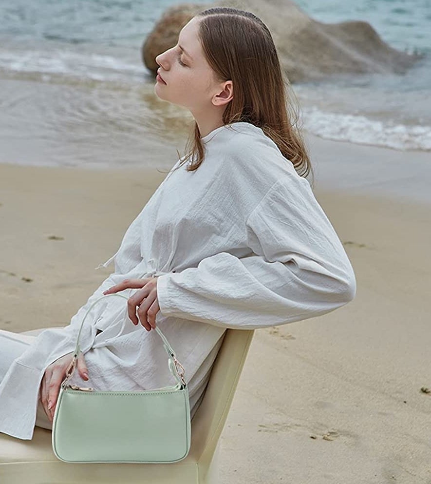 A person sitting on a beach holding the handbag