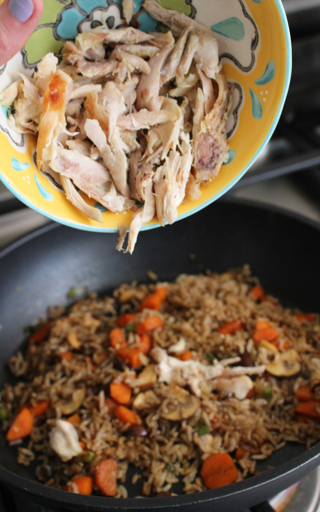 Pouring rotisserie chicken into a rice skillet.