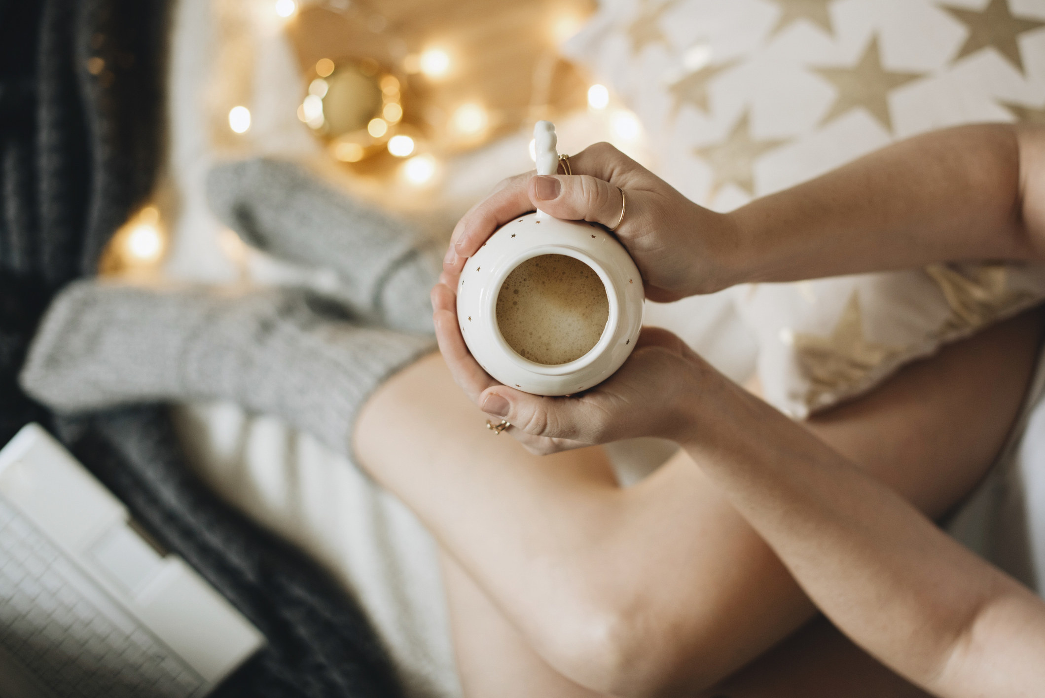 A girl holding a mug of coffee in bed.