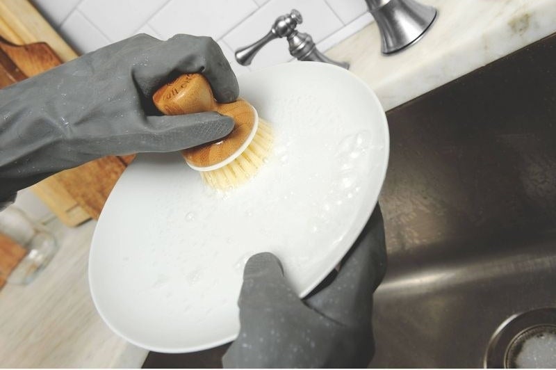 a person cleaning a white dish with a bubble up soap dispenser