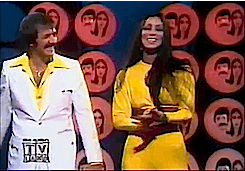 Sonny Bono laughing and clapping as Cher tosses her hair over her shoulders