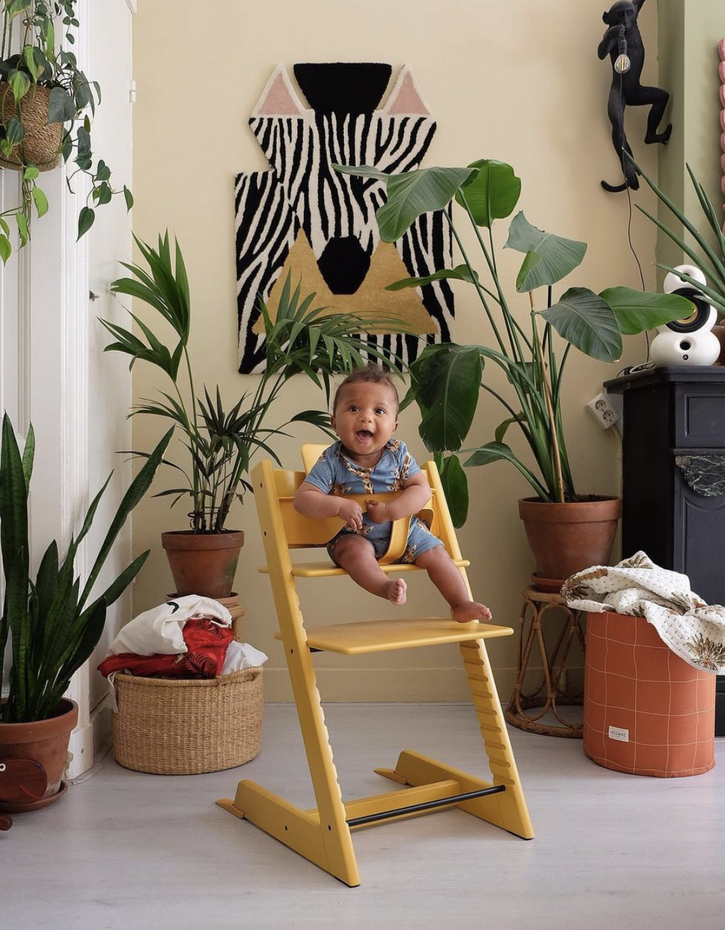 A cute baby sitting in a yellow Stokke high chair.