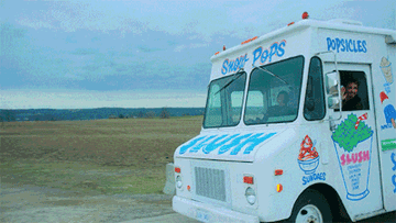 A GIF of a man driving past in an ice cream truck, waving at the camera