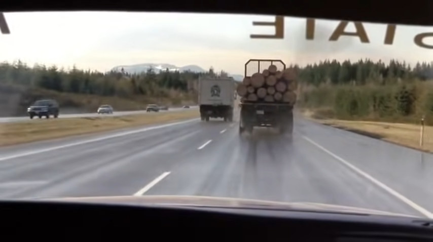 on the road, the driver is behind a large truck hauling lumber
