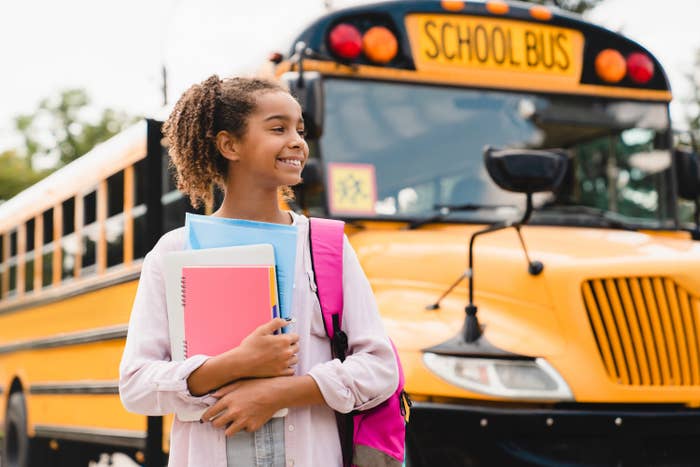 girl getting off the school bus with notebooks and a new backpack