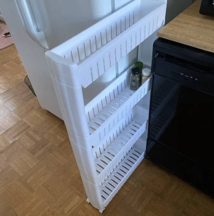 Reviewer's photo of the rack placed in space between fridge and countertop with three spices stored on second shelf
