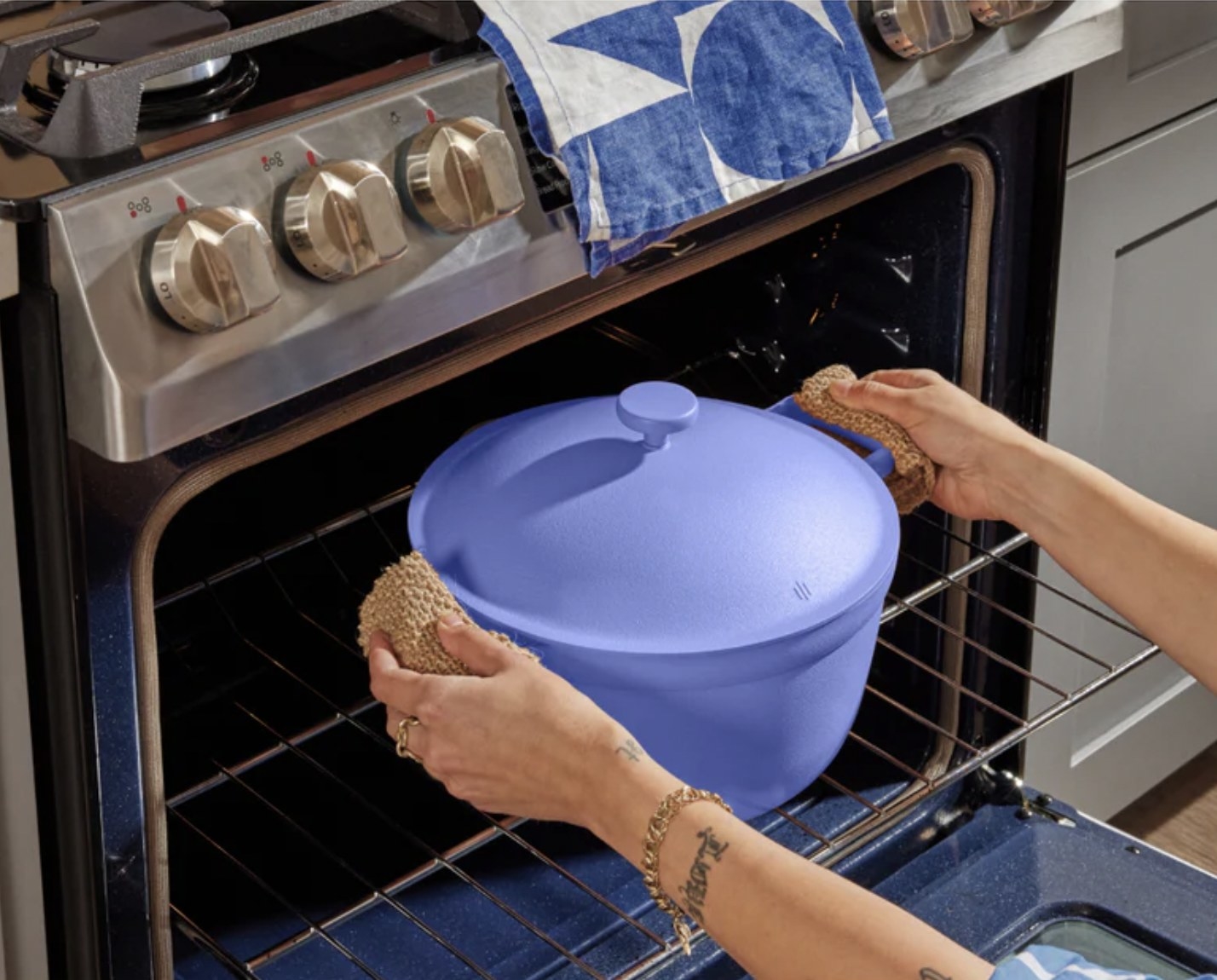 Someone using pot grips on the side handles as they put the blue pot into the oven
