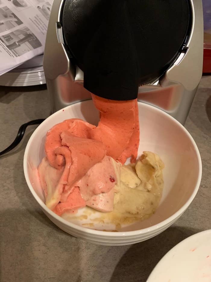 Reviewer&#x27;s photo of frozen fruit soft serve coming out of the maker into a bowl containing other flavors already