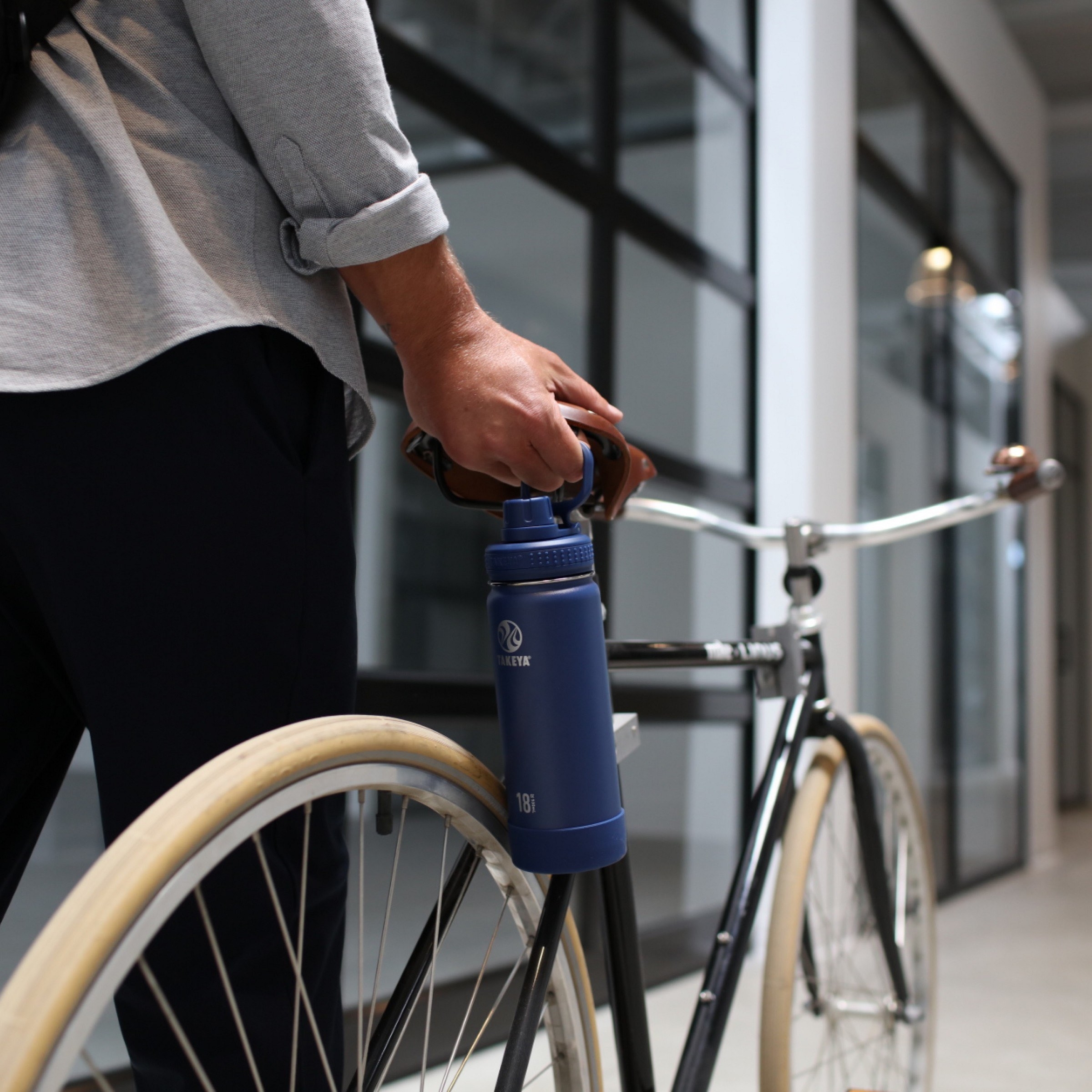 a model carrying the navy blue bottle while waking a bicycle