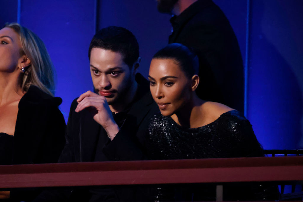 Pete Davidson and Kim Kardashian sitting at an event and looking over a railing