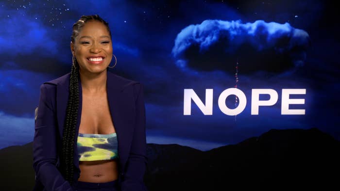 Keke Palmer in an interview setting with the nope film poster in the background