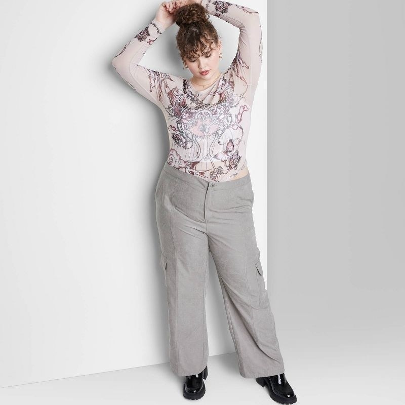 A model wearing a white and pink top with grey pants and black shoes