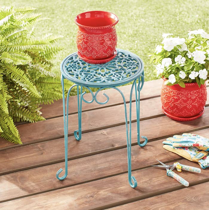 teal four-leg metal plant stand with a red pot on it