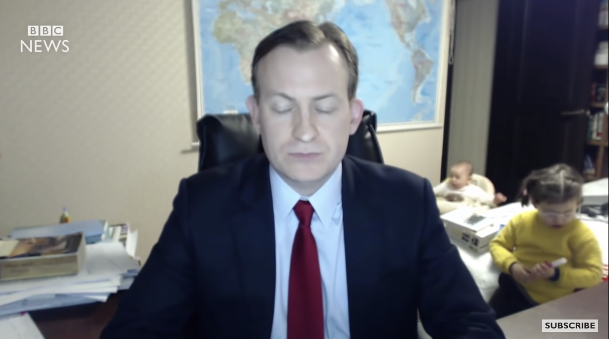 a man sat at his desk during a video call with his two children in the background