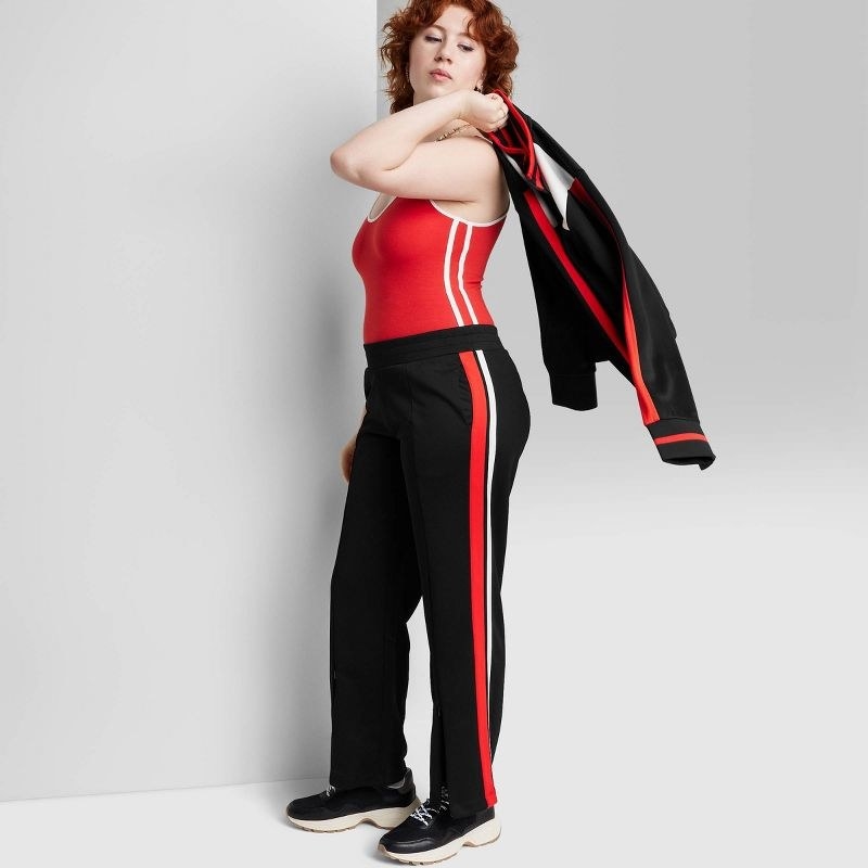 Model wearing black, red and white pants, with black sneaker and a red and white striped body suit