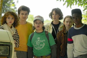 Nancy, Steve, Dustin, Robin, Max, and Lucas from Stranger Things standing outside and looking ahead