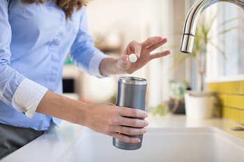 model placing small white Bottle Bright tablet into stainless steel tumbler