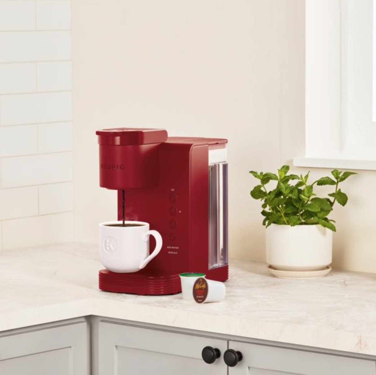 the small red coffee maker on a counter with a plant