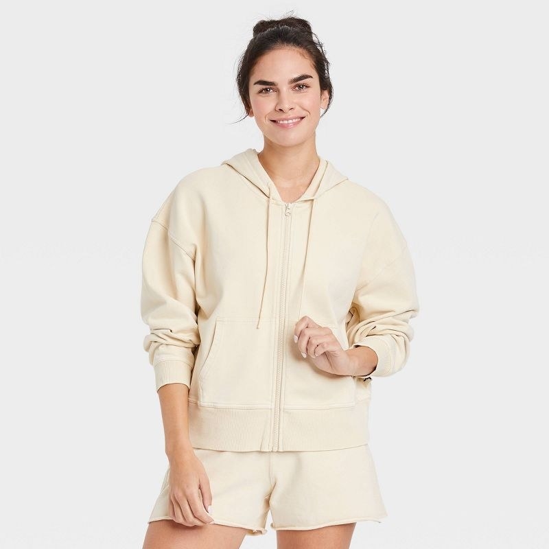 Model wearing cream zip-up hoodie and matching shorts