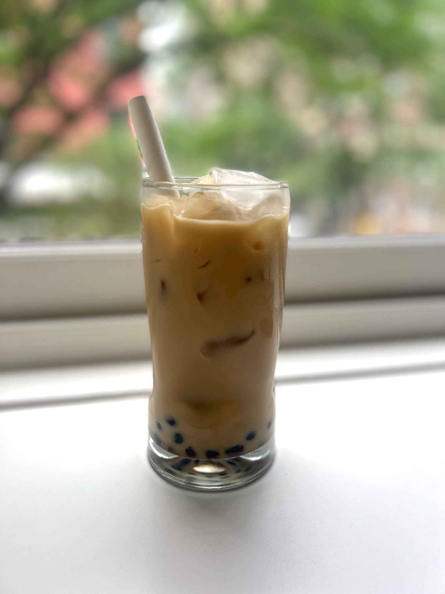 A glass of boba tea on a windowsill.