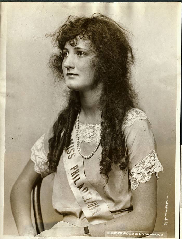 Ruth Malcolmson, wearing a Miss Philadelphia sash, sits wearing a long pearl necklace and long, curly hair with pigtails