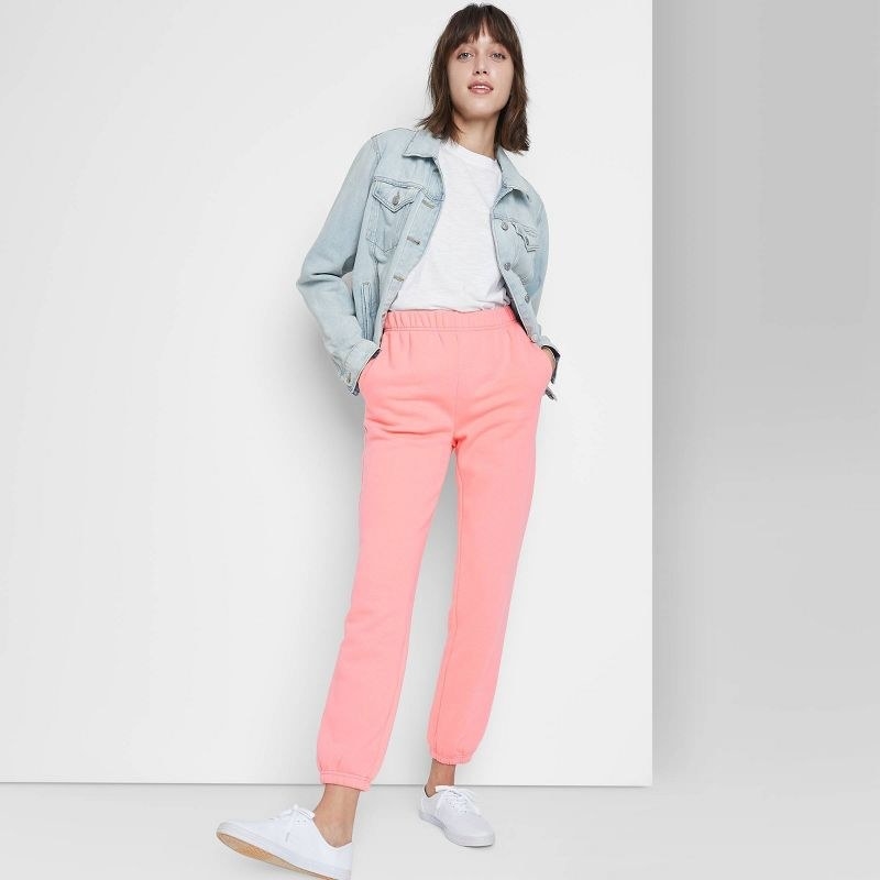 A model wearing pink pants, white sneakers, white tee and light denim jacket