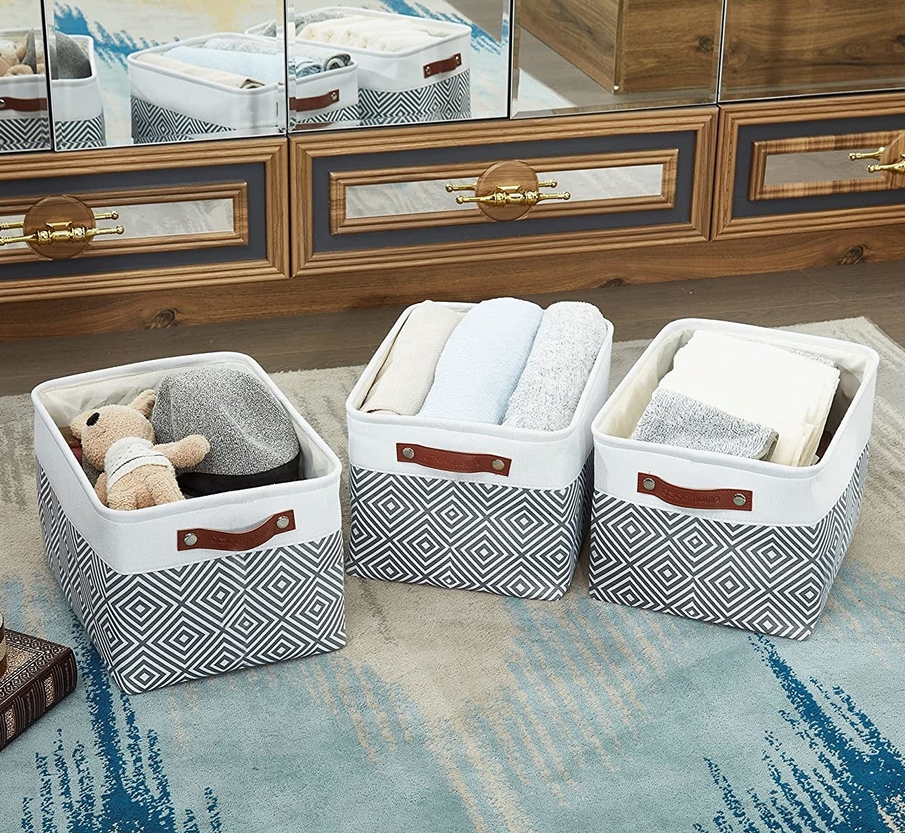 three fabric baskets on a floor filled with blankets, towels, and toys