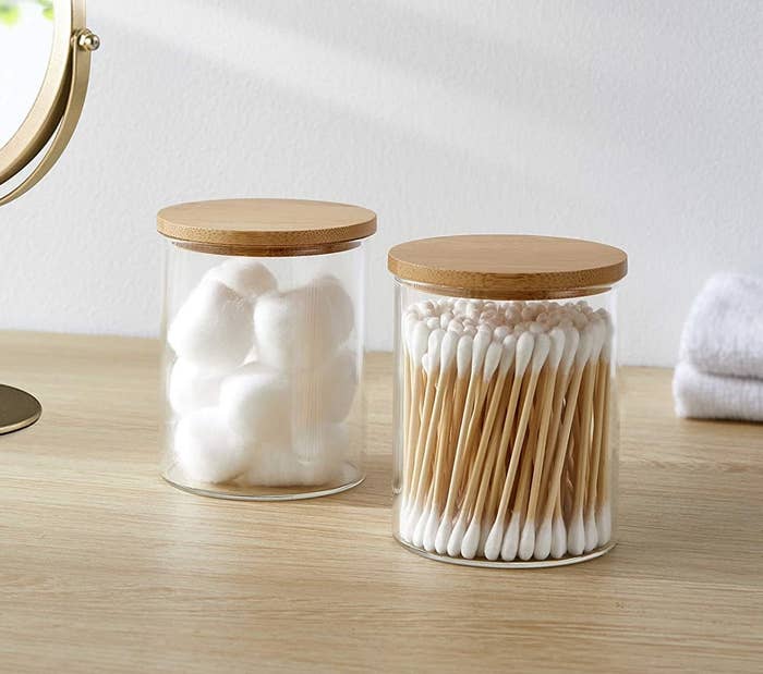 two glass jars with bamboo lids with cotton balls in one and cotton swabs in the other