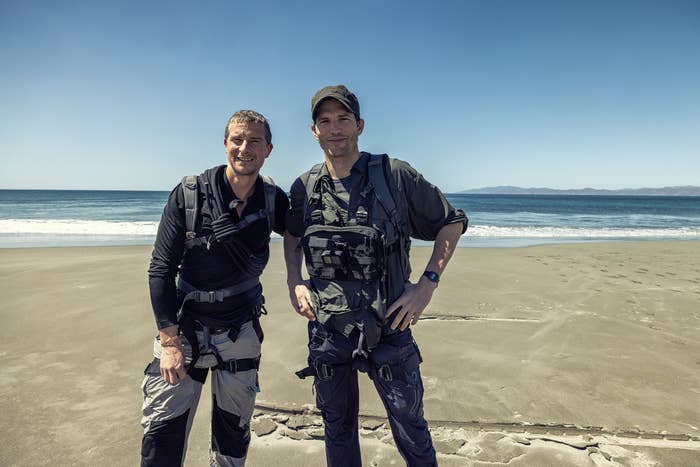 Two men wearing harnesses on their chests stand side by side on a beach