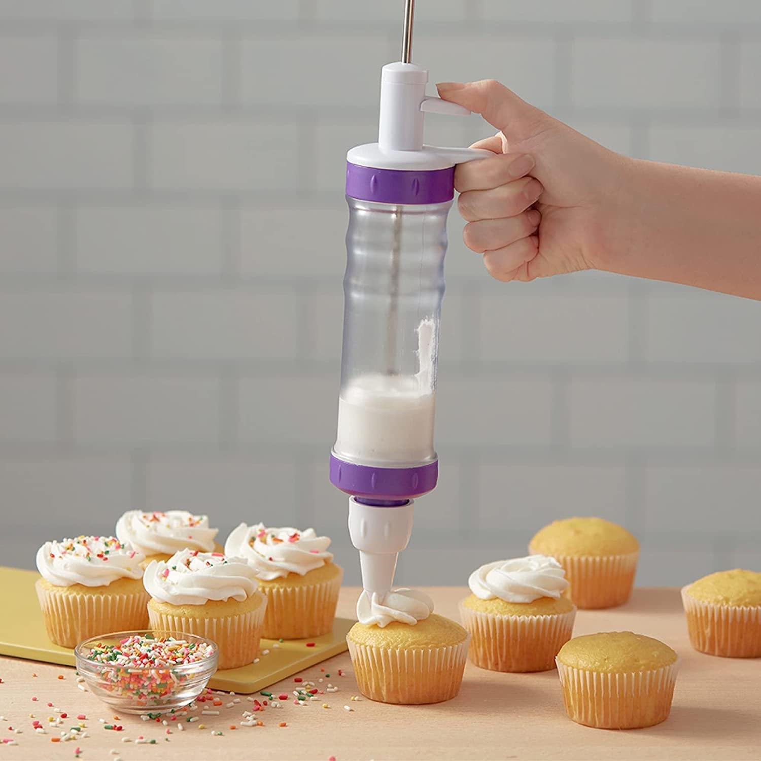 A person using the tool to pipe frosting onto a cupcake