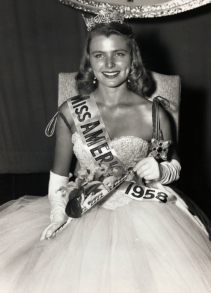 Van Derber in a gown and her crown, sitting