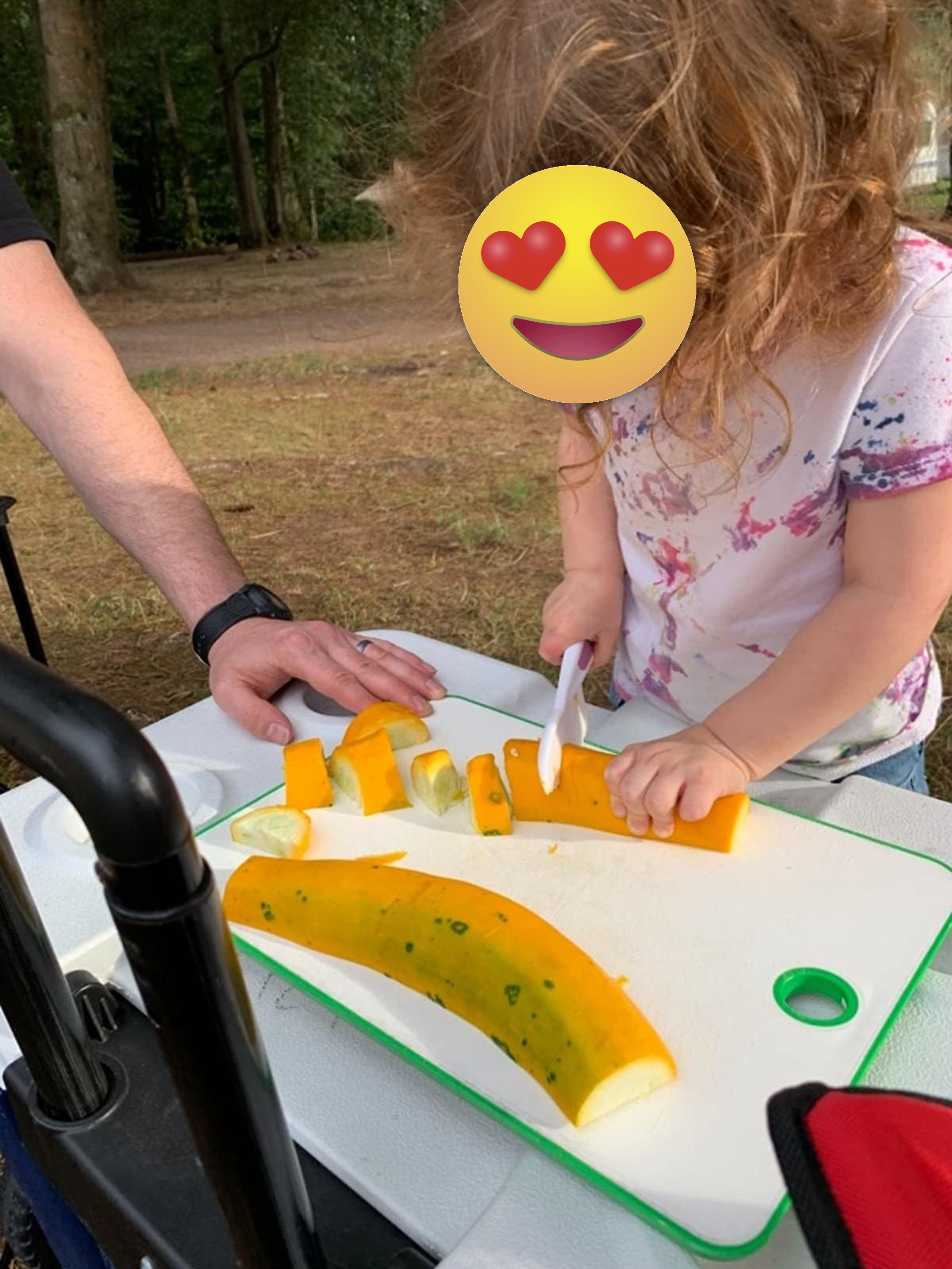Reviewer&#x27;s kid using the white plastic knife to chop a summer squash on a cutting board outside
