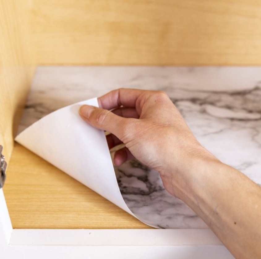 Arm applying marble contact paper to wooden shelf