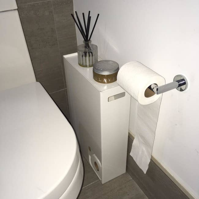 reviewer image of the white rectangle holder with a small square cut out in the bottom left corner, revealing rolls of toilet paper inside