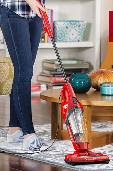 A person pushing the vacuum on a floor in a living room