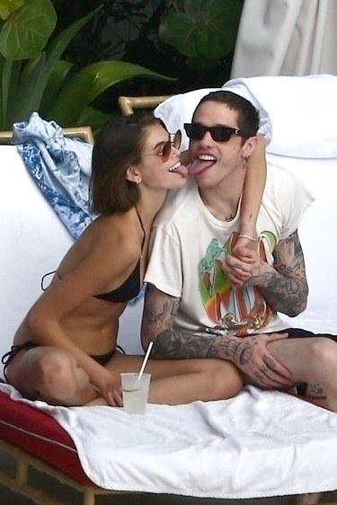 Kaia Gerber and Pete in swimsuits touching tongues on lounge chairs