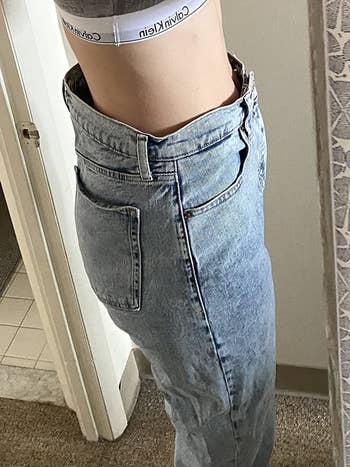 reviewer pic of reviewer wearing baggy blue jeans with waist gap