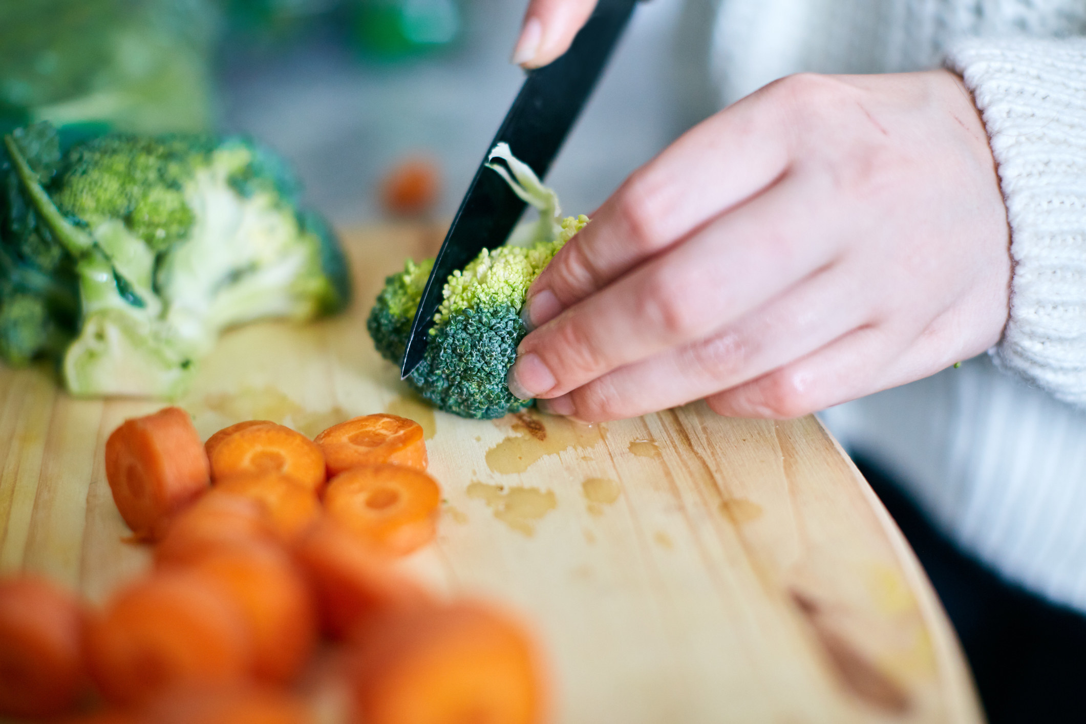 Woman&#x27;s hand slicing broccoli on wooden chopping board.