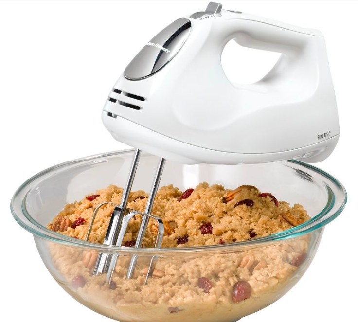 White hand mixer being used to mix cookie dough in a glass bowl