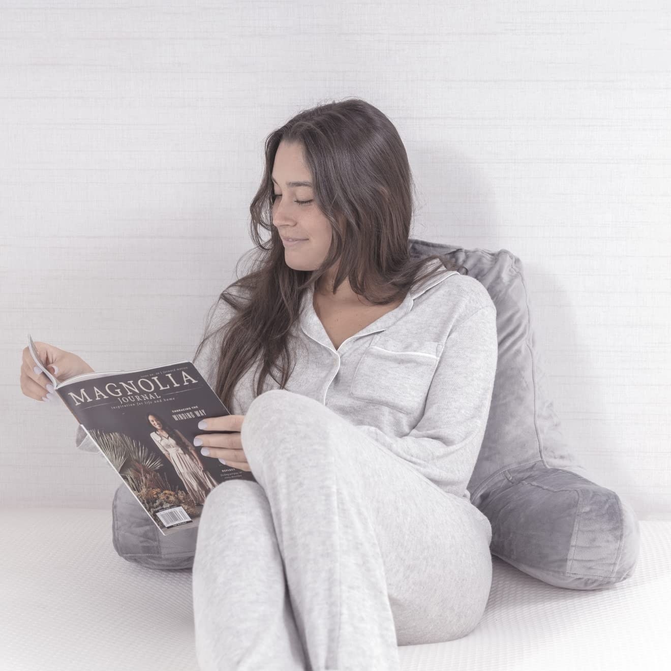 a person reading a magazine while laying on their reading pillow