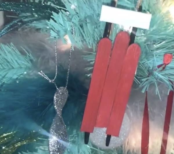 Ice-pop sticks stuck together to look like sleds are hung from a tree as ornaments