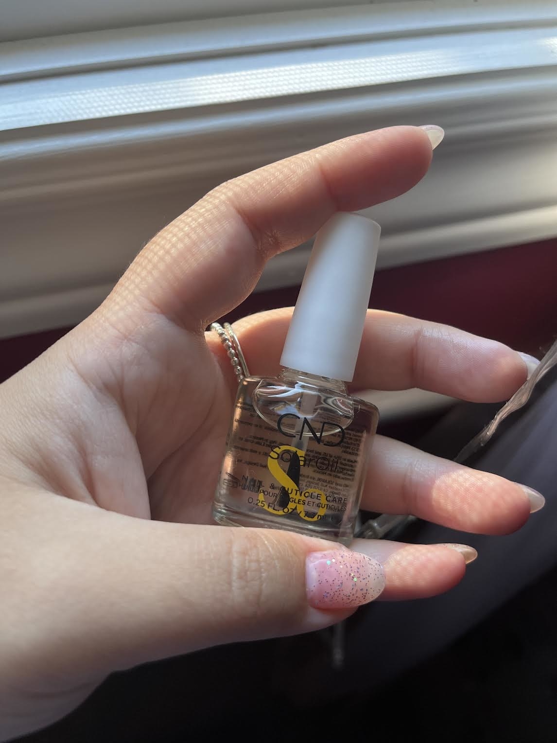 Bianca holding up the cuticle oil in front of a window