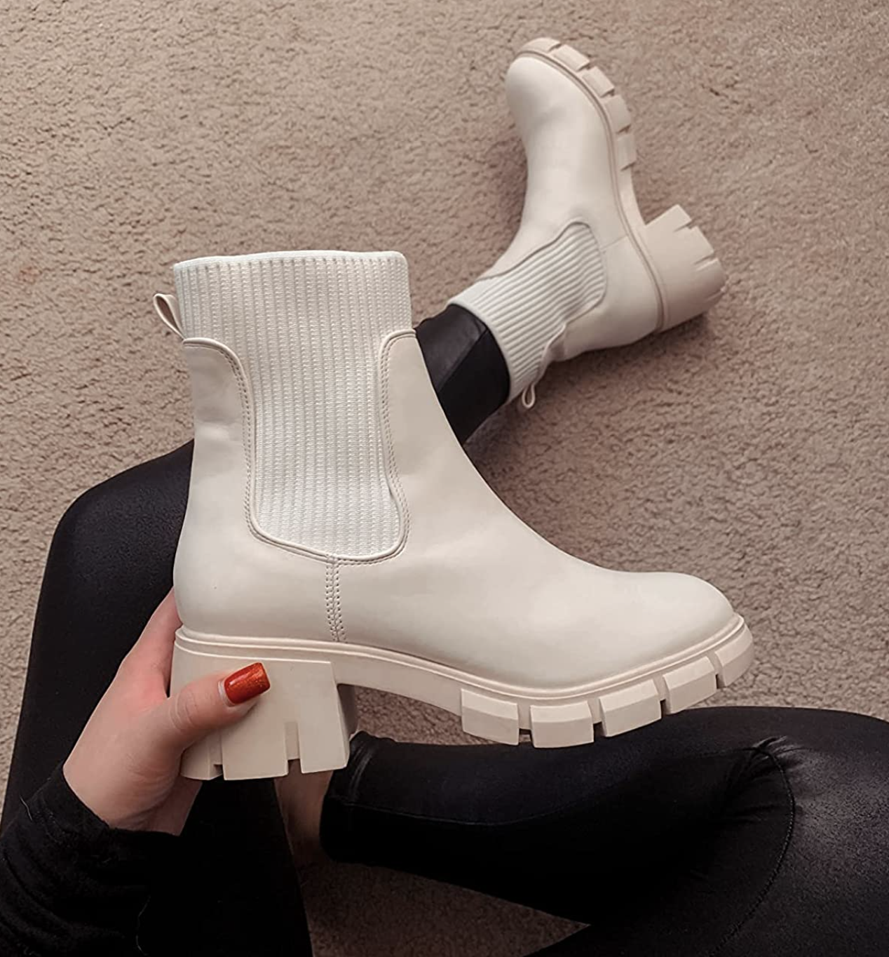 a hand holding the pair of white elastic ankle chelsea boots