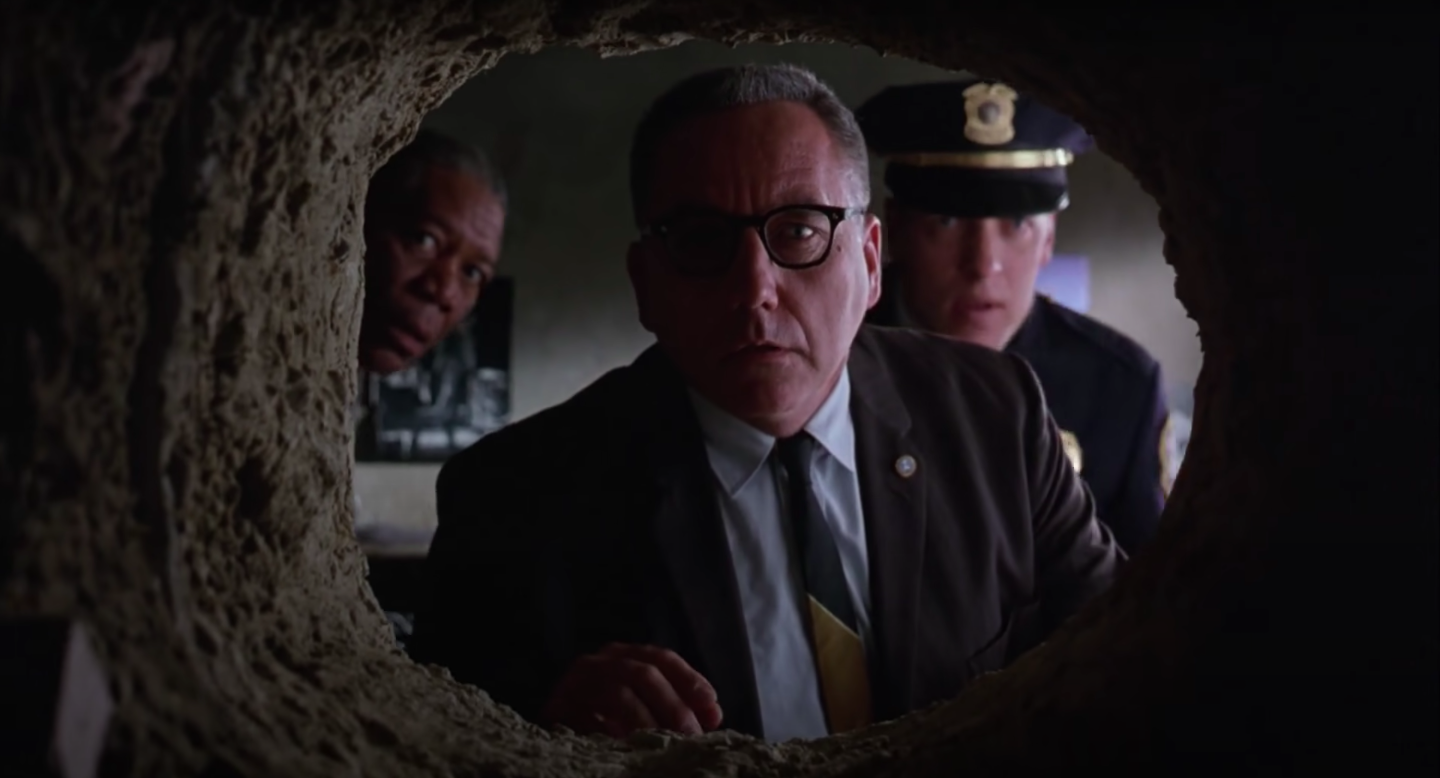 A group of men look through a large hole dug into a wall