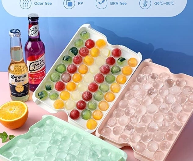 a set of the ice trays on a table beside bottles and cut fruit