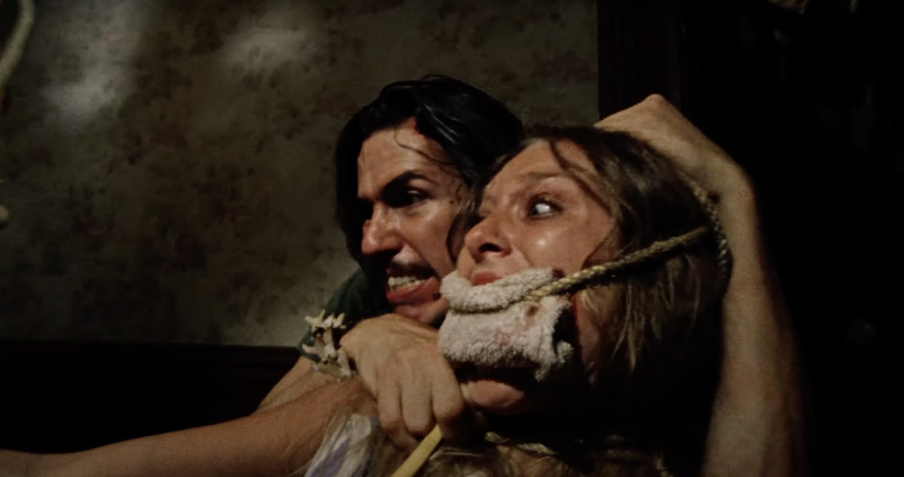 Man holding the head of a woman with a gag in her mouth