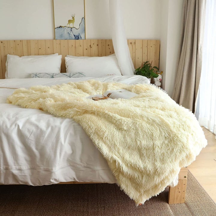 the light yellow throw blanket on the end of a bed