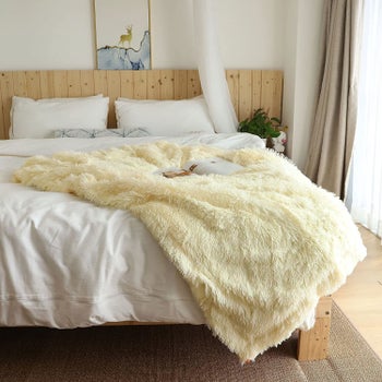 the light yellow throw blanket on the end of a bed
