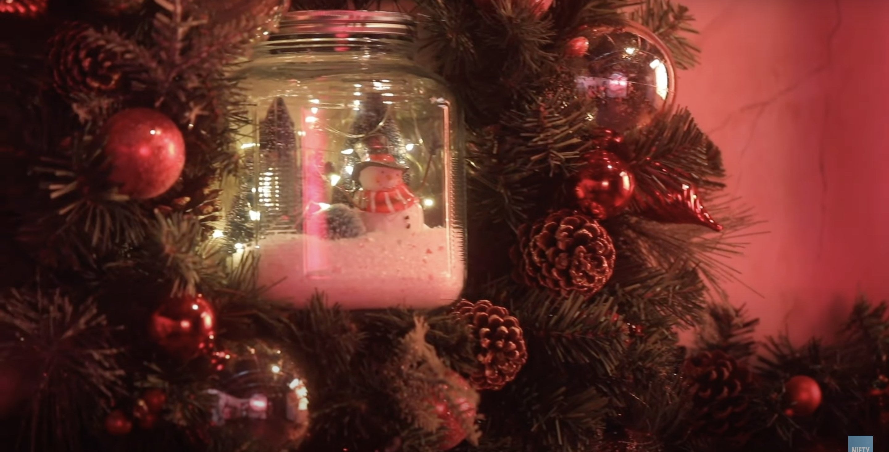A Mason jar in the middle of a wreath with a Christmas tree and snowman scene